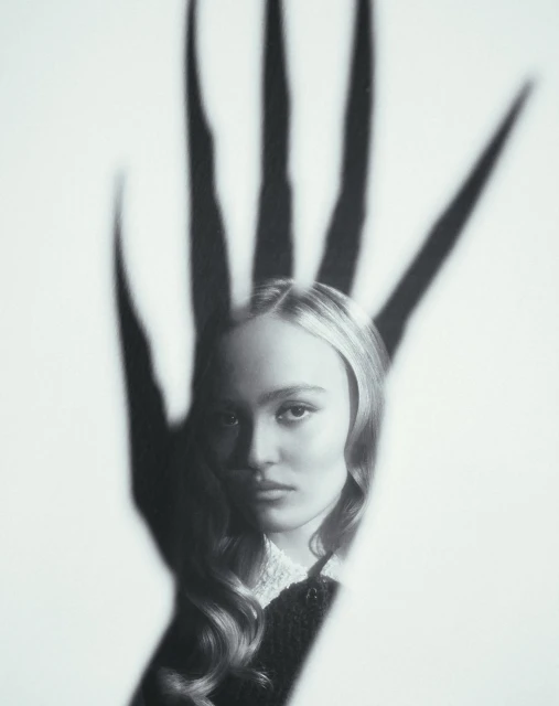 Monochrome portrait of a young woman with long wavy hair and a shadow of a hand with long fingers over her face on white.