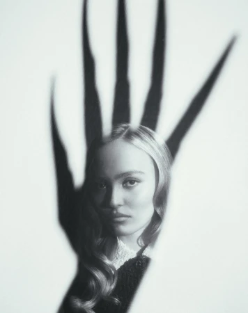 Monochrome portrait of a young woman with long wavy hair and a shadow of a hand with long fingers over her face on white.