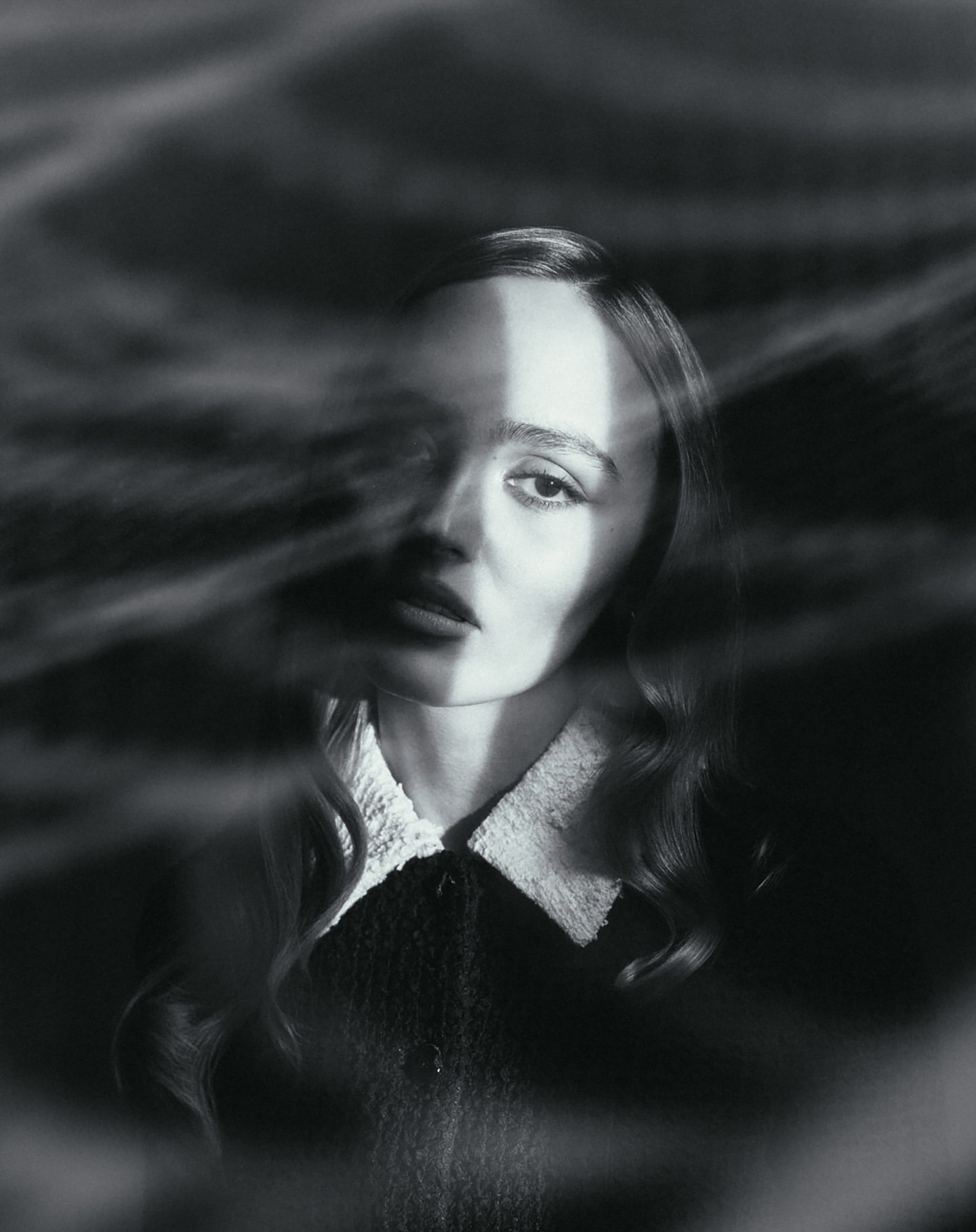 Black and white portrait of a woman with dark wavy hair wearing a collared dress, viewed through a textured semi-transparent overlay.