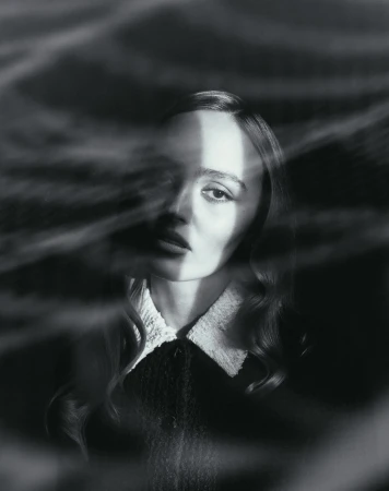 Black and white portrait of a woman with dark wavy hair wearing a collared dress, viewed through a textured semi-transparent overlay.