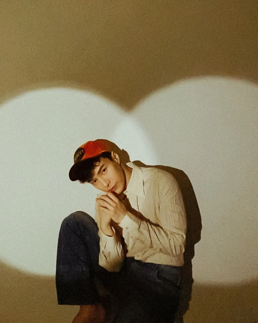 Portrait of a young adult man with brown hair, wearing a red baseball cap, a white shirt, and jeans, posing in a photo studio.