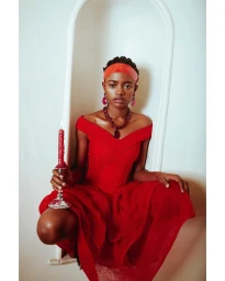 Woman in red dress crouching inside a white arched alcove holding a lit red candle