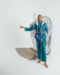 A man in a teal outfit wearing a large transparent plastic structure against a white background