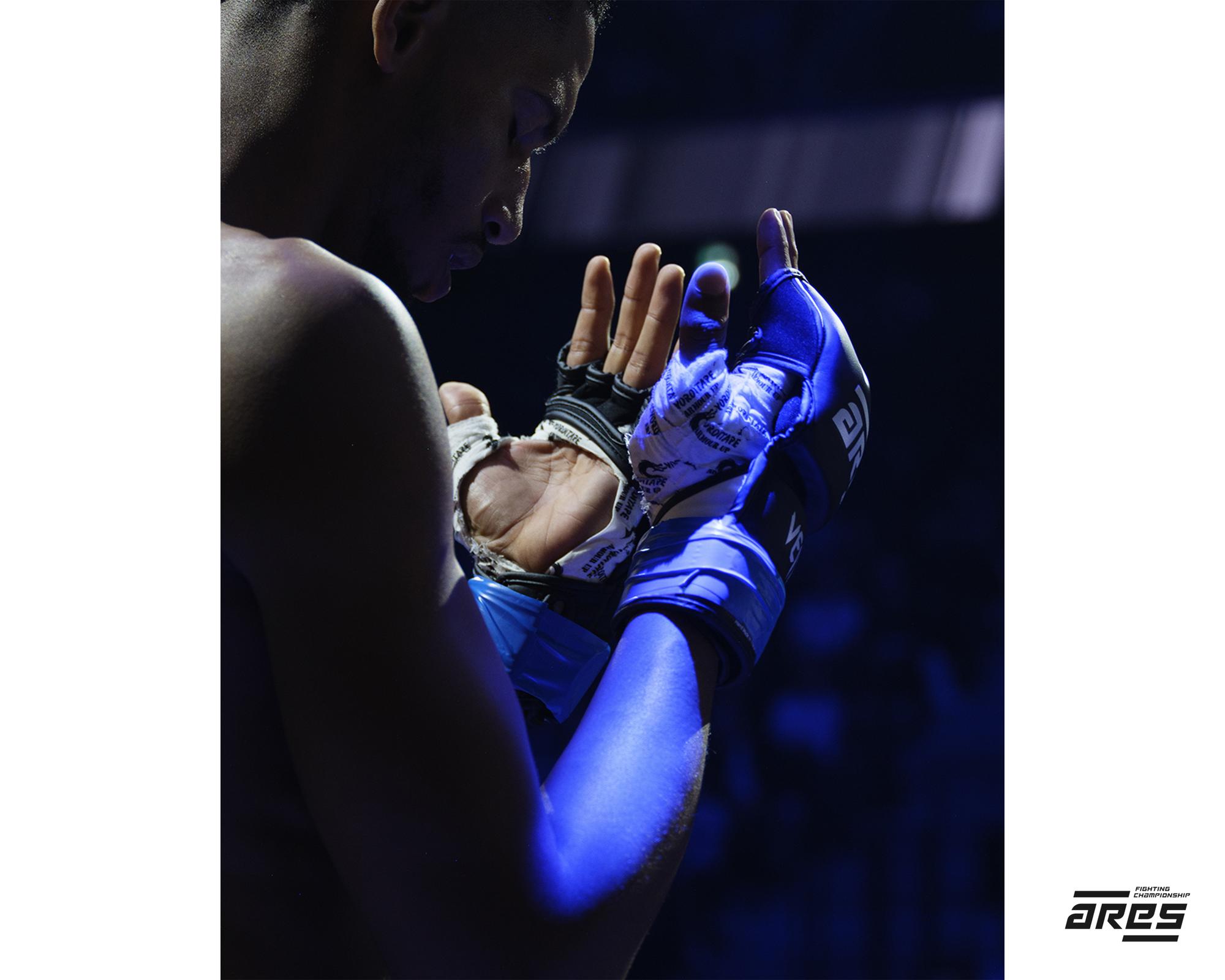 Close-up of a male MMA fighter with hands wrapped and gloved in a fighting stance, blue gel lighting.