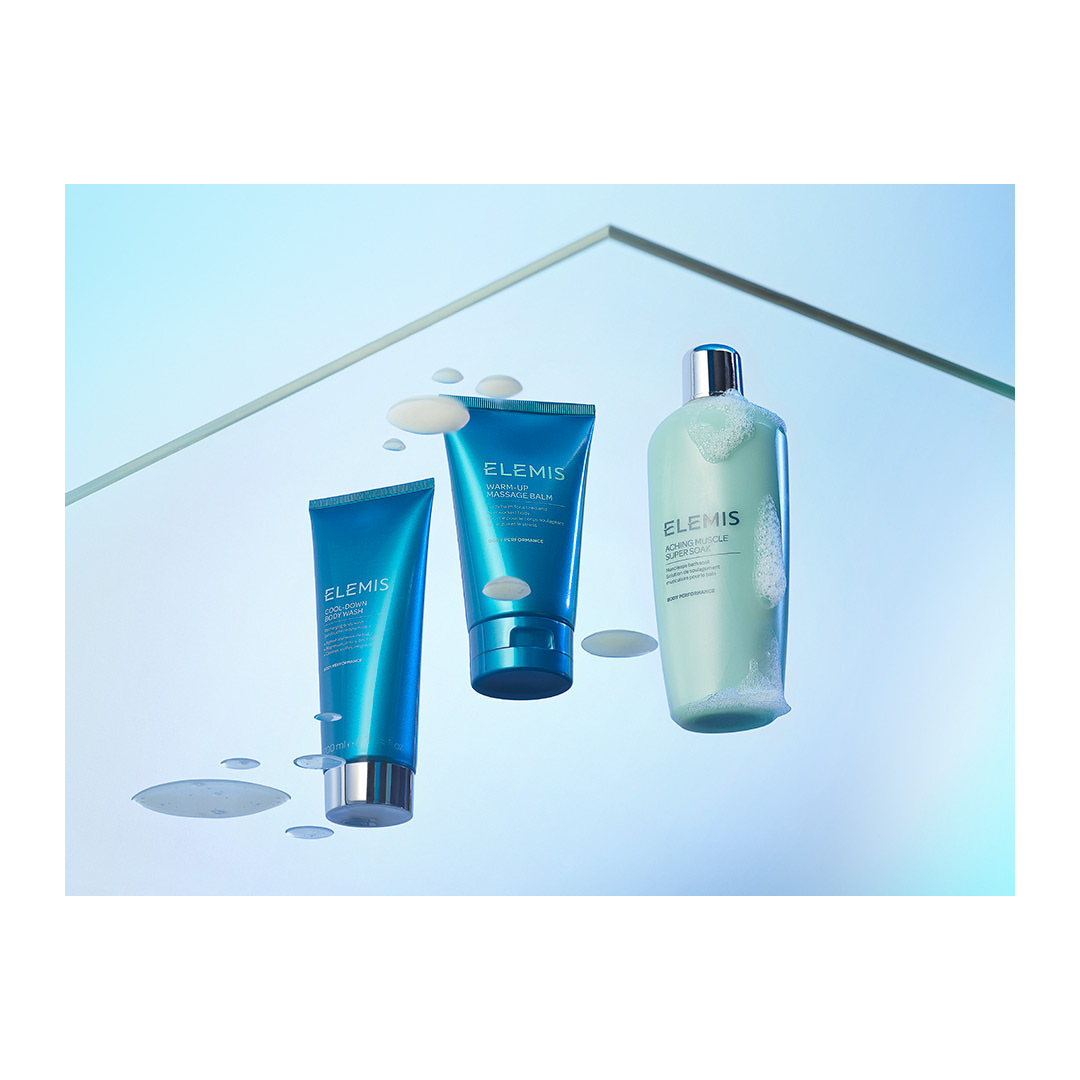 Three Elemis brand skincare products, including facial wash, arranged against a light blue backdrop with a geometric transparent shelf.