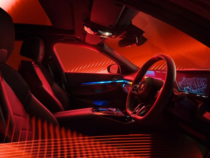 Car interior with steering wheel, dashboard display, and illuminated accents under a red lighting scheme, showcasing modern automotive design.