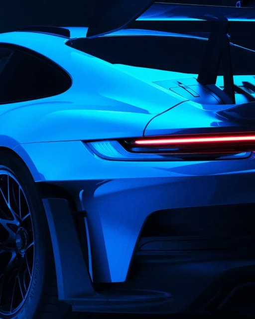 Rear view of a sleek blue sports car, showcasing its aerodynamic design and red taillight against a dark background, with visible wheel detail.