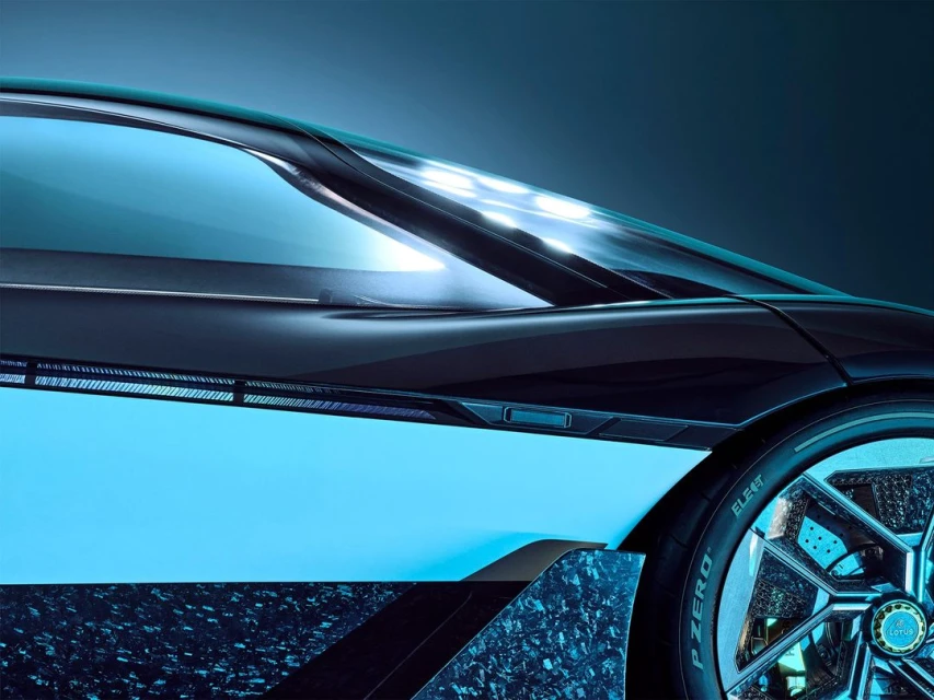The side of a dark blue Lotus sports car with glowing lights is captured in a closeup shot showcasing its unique wheel design.