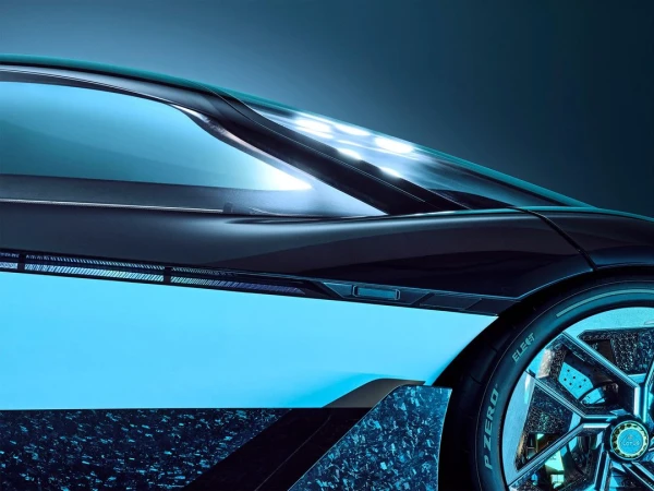 The side of a dark blue Lotus sports car with glowing lights is captured in a closeup shot showcasing its unique wheel design.