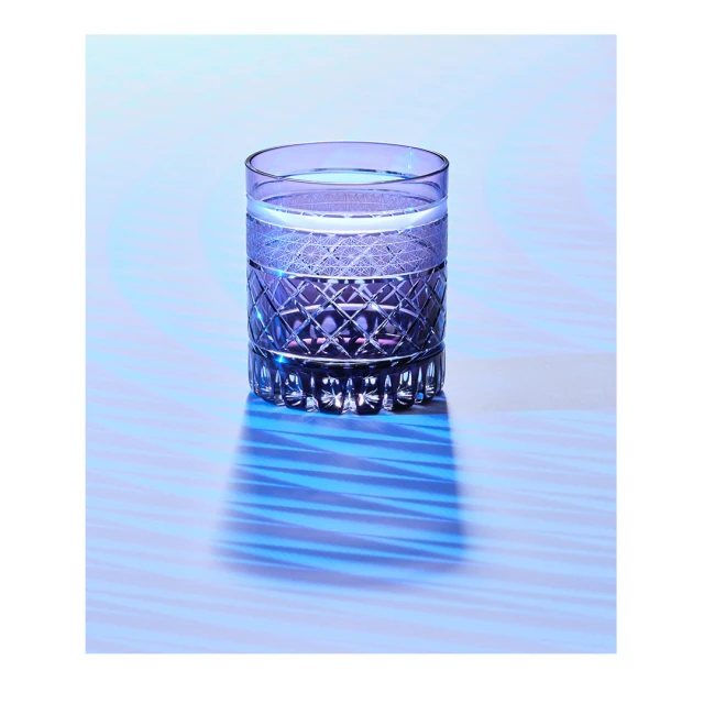 Crystal glass filled with liquid on a light blue surface casting a shadow, simple product-style shot, advertising or promotional still life.