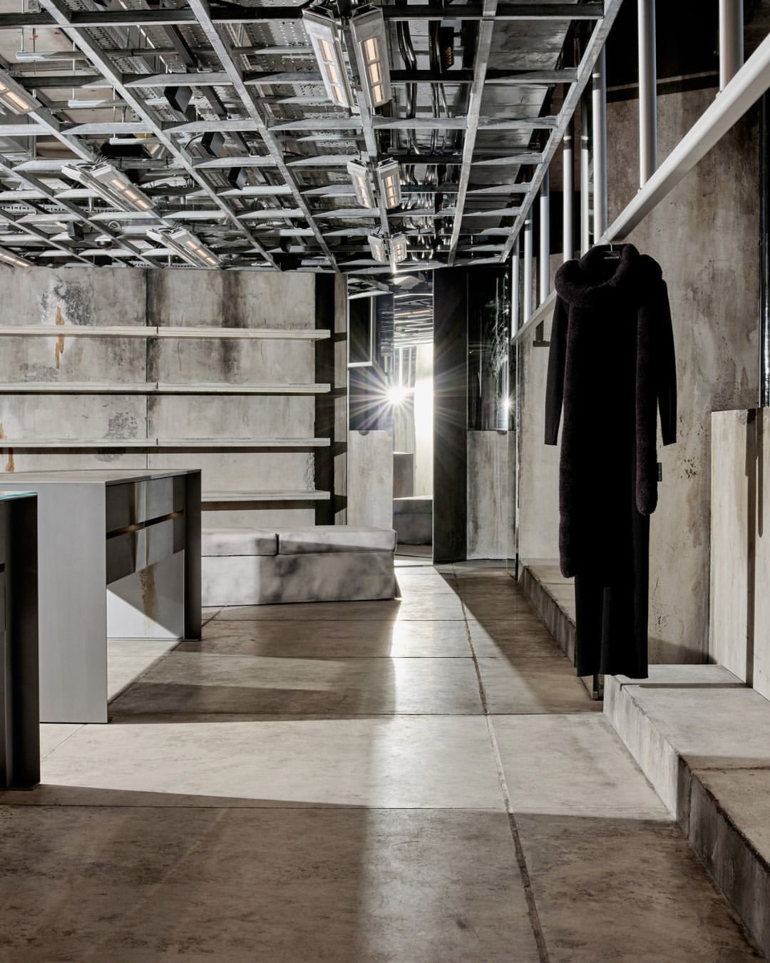 Interior of a modern store with a hooded coat hanging on a rack, concrete floors and walls, and metal ceiling framework with lights.
