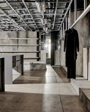 Interior of a modern store with a hooded coat hanging on a rack, concrete floors and walls, and metal ceiling framework with lights.
