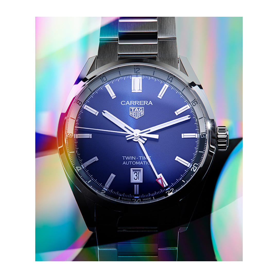 Luxury TAG Heuer Carrera watch close-up on a metal bracelet with a blue dial and iridescent background, showcasing its elegant design.