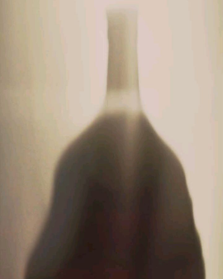 Elegant photo of a tall, dark-colored bottle, possibly containing wine or liquor, set against a soft, diffused background.