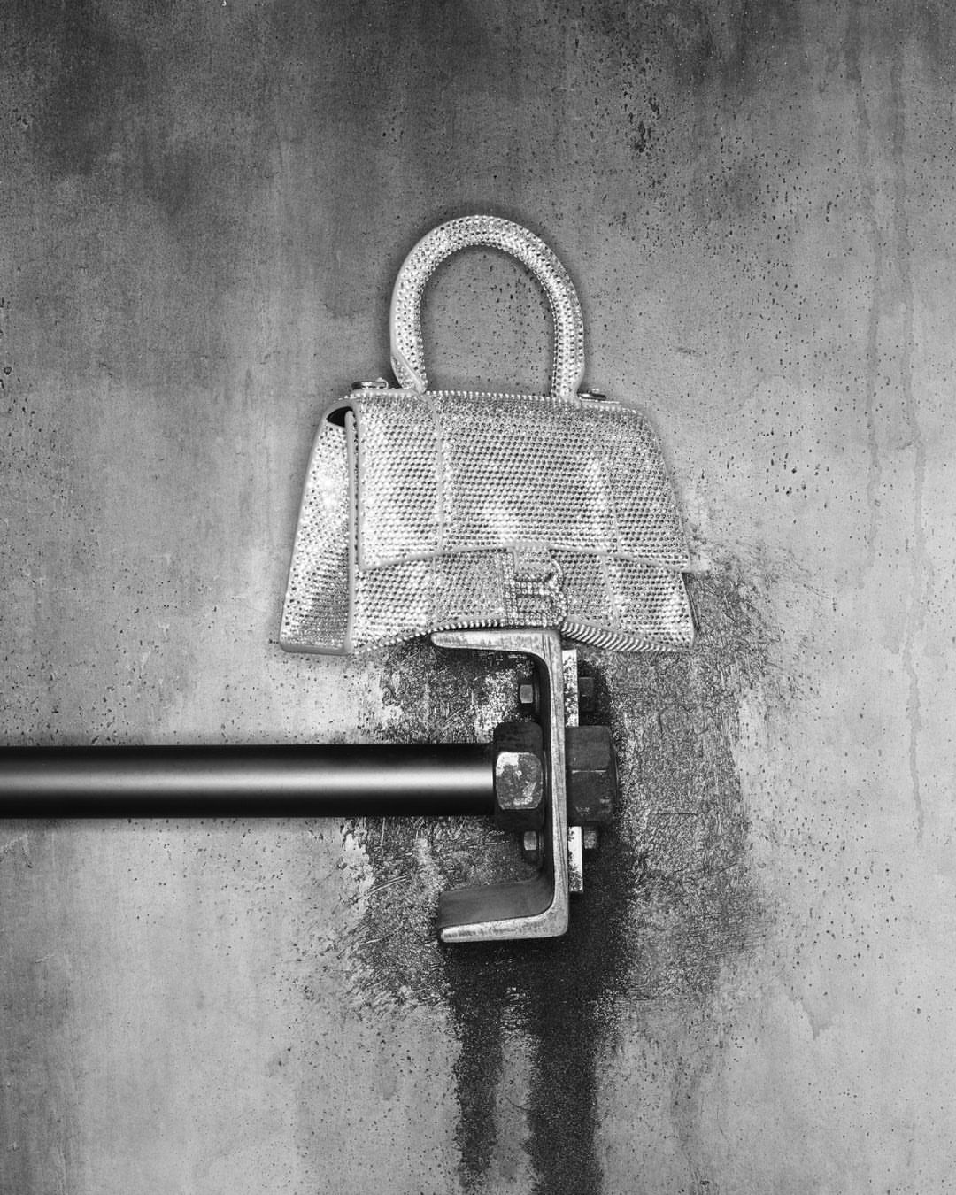 Fashion-forward purse spotlight: a gleaming, studded handbag mounted on a metallic bar against a textured concrete backdrop.