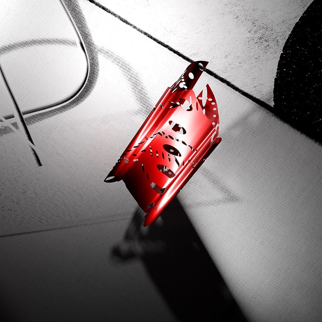 Abstract product shot of a red, geometrically-patterned object on a textured, grayscale surface, highlighted by a strong shadow.