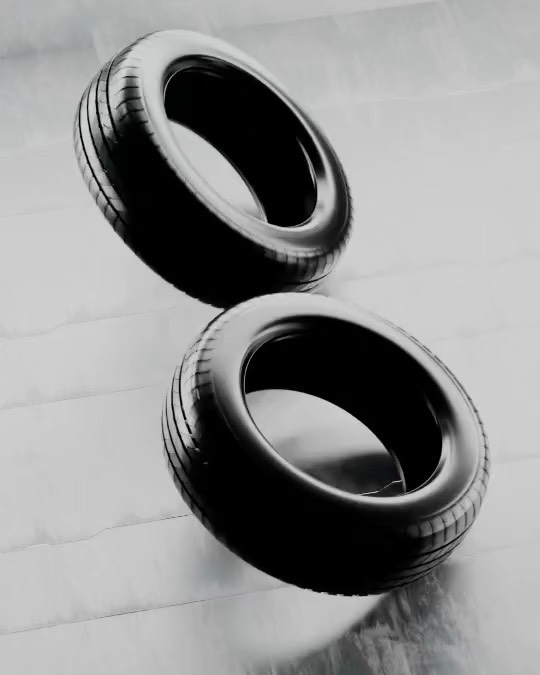 Two black car tires stacked diagonally on a light gray surface, showing tire treads and sidewalls in studio product shot.