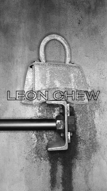 Close-up of a reflective, jeweled purse displayed on a metal fixture against a grey textured background with black 'LEON CHEW' text.