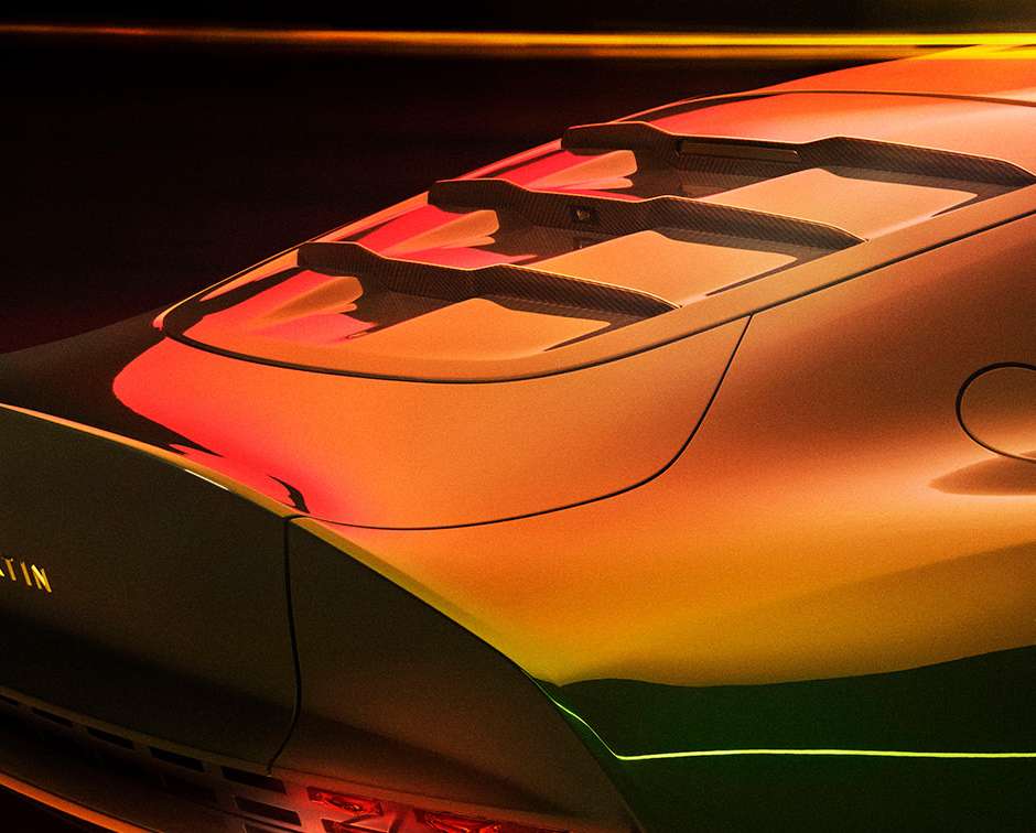 Close-up of the rear of a modern orange and black Aston Martin car with visible taillights, vents, and brand badging on a dark backdrop.