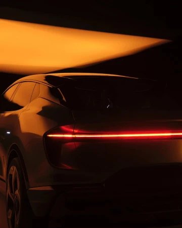 Rear view of a modern silver car with a horizontal red light bar, set against a dark background with soft orange lighting.