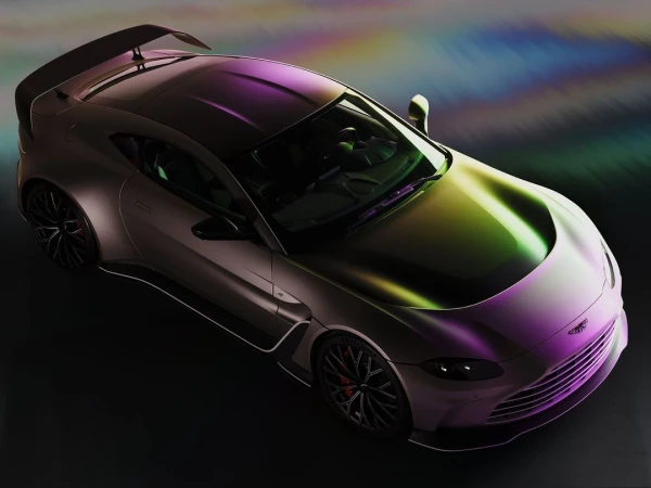 An overhead studio shot showcases a gray Aston Martin Vantage with a rear spoiler, featuring reflections of purple, green, and yellow light.