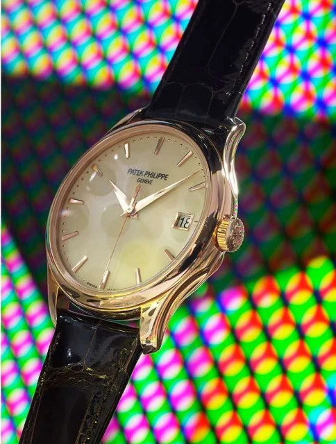 Elegant gold Patek Philippe watch with a black leather strap displayed against a colorful patterned background. Close-up studio shot.