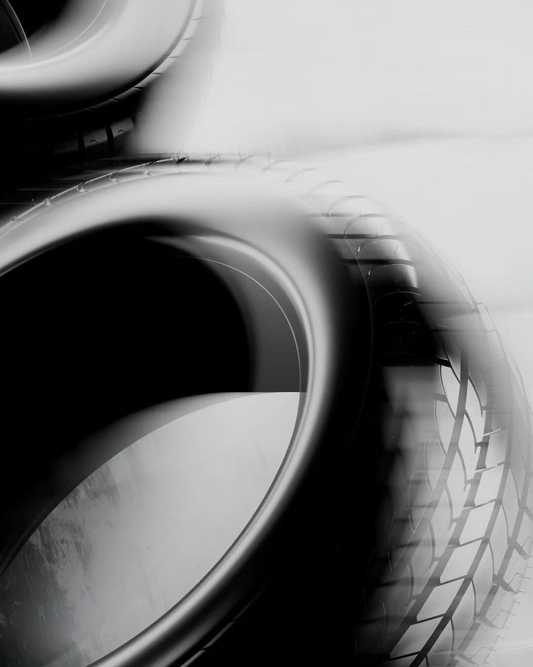 Monochrome image of stacked car tires, showcasing tire treads and circular forms in a high-contrast, abstract automotive aesthetic.