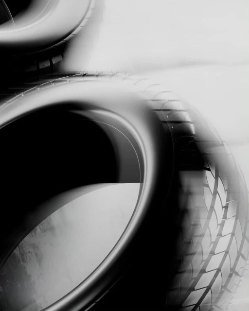 Monochrome image of stacked car tires, showcasing tire treads and circular forms in a high-contrast, abstract automotive aesthetic.