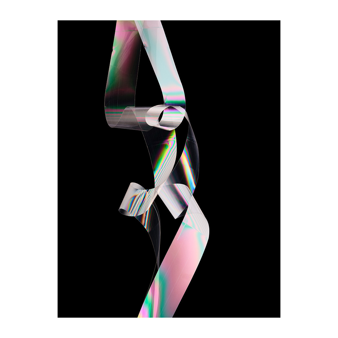 Abstract studio shot of a transparent ribbon with iridescent reflections, illuminated against a black background for an artistic visual.