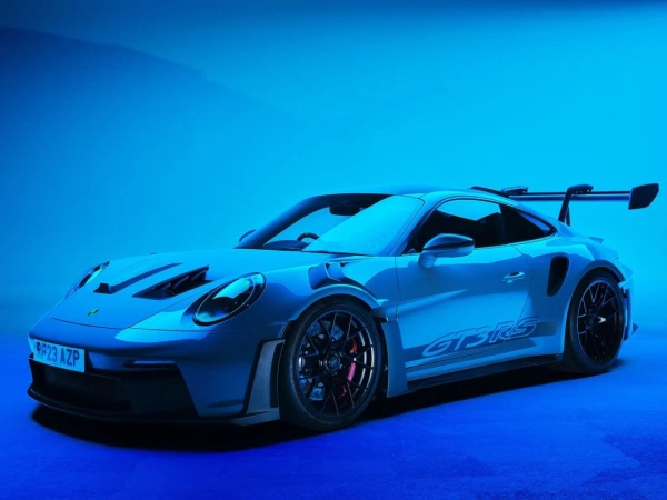 Sleek, blue Porsche GT3 RS sports car showcased in a studio setting with vivid blue lighting, highlighting its aerodynamic design.