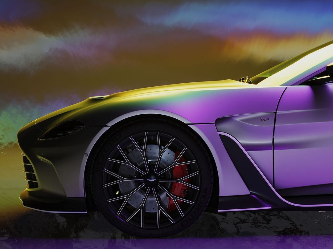 Close-up of an Aston Martin Vantage showcasing a sleek, silver exterior, intricate black wheel design, and vibrant red brake calipers, studio shot.