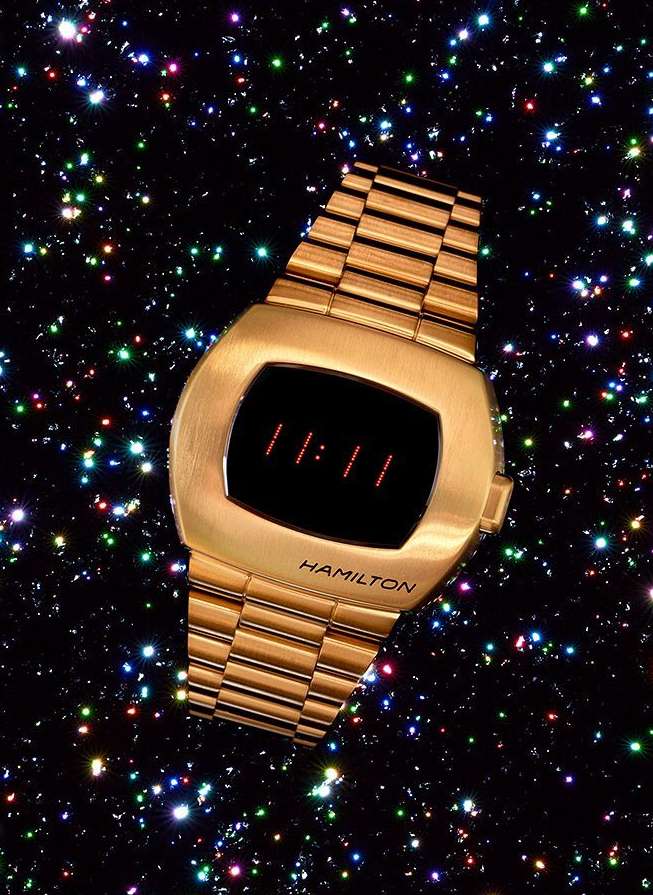 Gold Hamilton Pulsar watch displaying '11:11' on a digital display against a bokeh background with colorful spots of light in the dark.