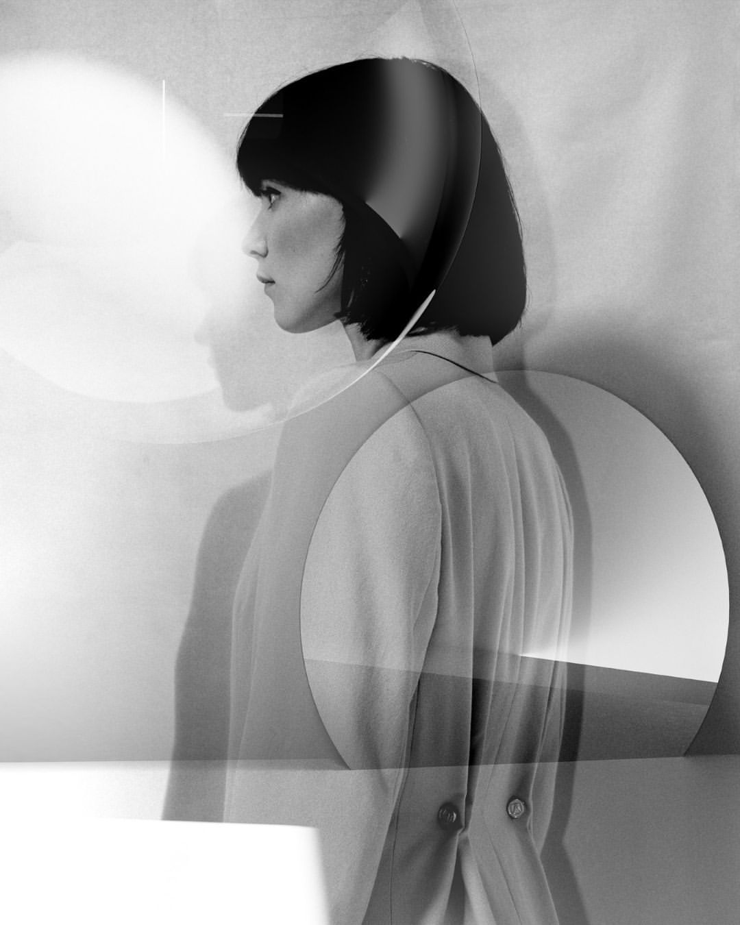 Monochrome portrait of a stylish Asian woman in profile with geometric overlay, standing indoors with muted tones and artistic lighting.