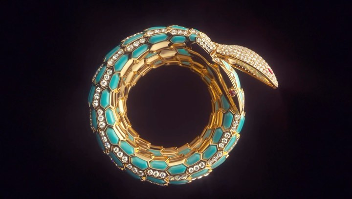 Close-up of a gold coil bracelet with turquoise gemstones and diamond embellishments on a dark background, styled as a snake.