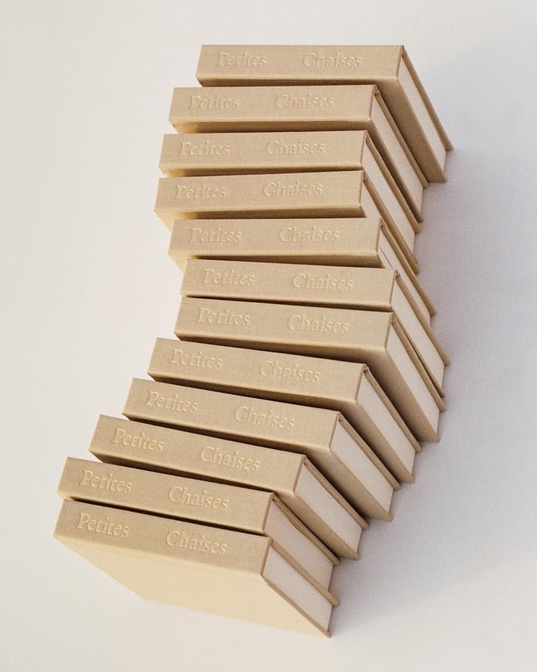 Stack of rectangular boxes with text 'Petites Chaises' in an alternating, zig-zag pattern against a plain, light background.
