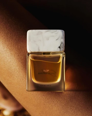 A rectangular perfume bottle with a white marble cap resting against skin in warm lighting