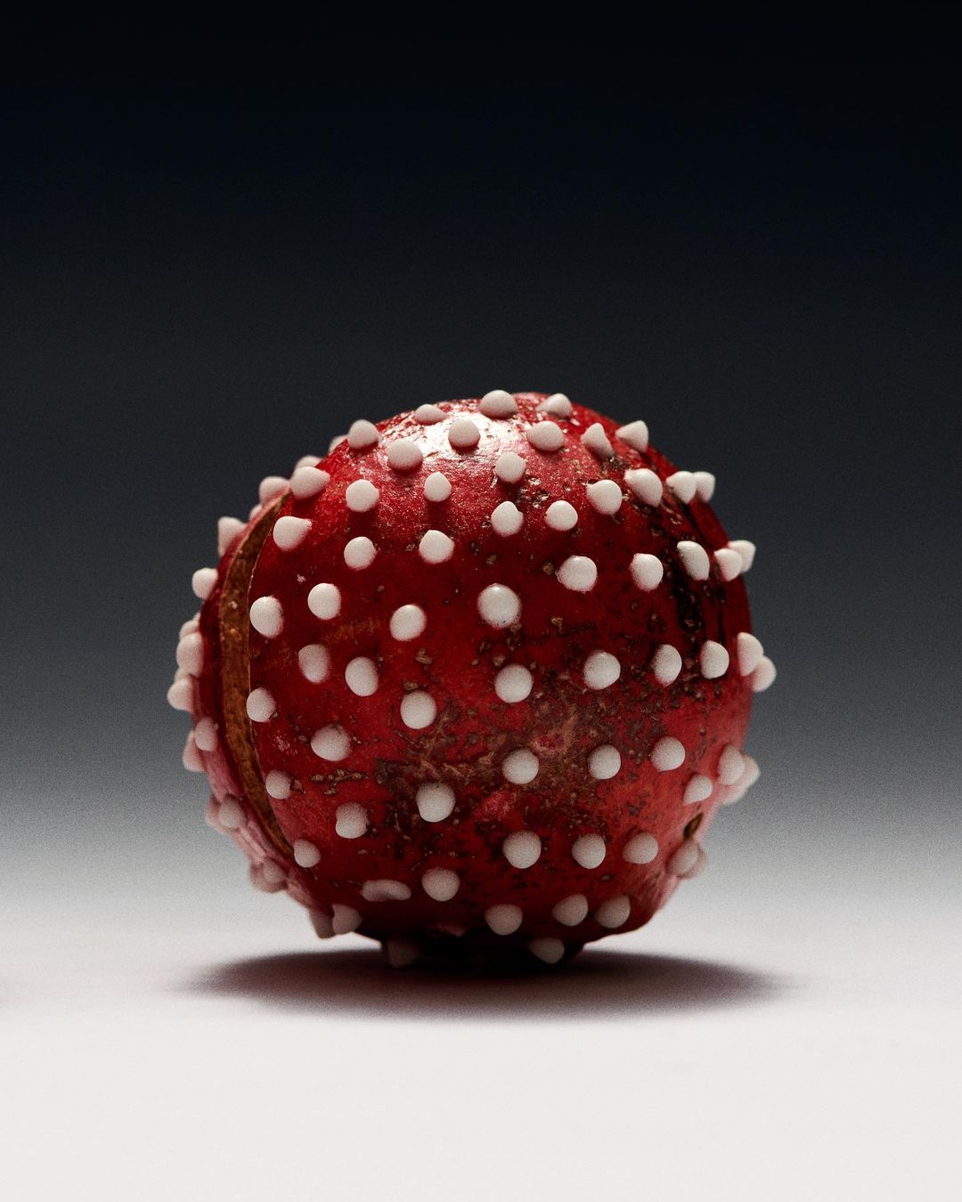 Close-up of a red glass bead with white dots, lit by studio lights against a dark gray background. Decorative object, handcrafted.
