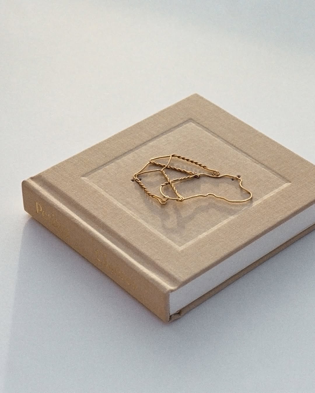 Gold chain necklace on top of a square, beige-covered book with white pages. The setting is minimalist and well-lit.