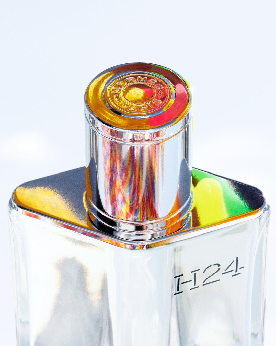 Close-up studio shot of a Hermès H24 Eau de Toilette bottle with a metallic silver cap, showcasing its modern design and reflective surface.