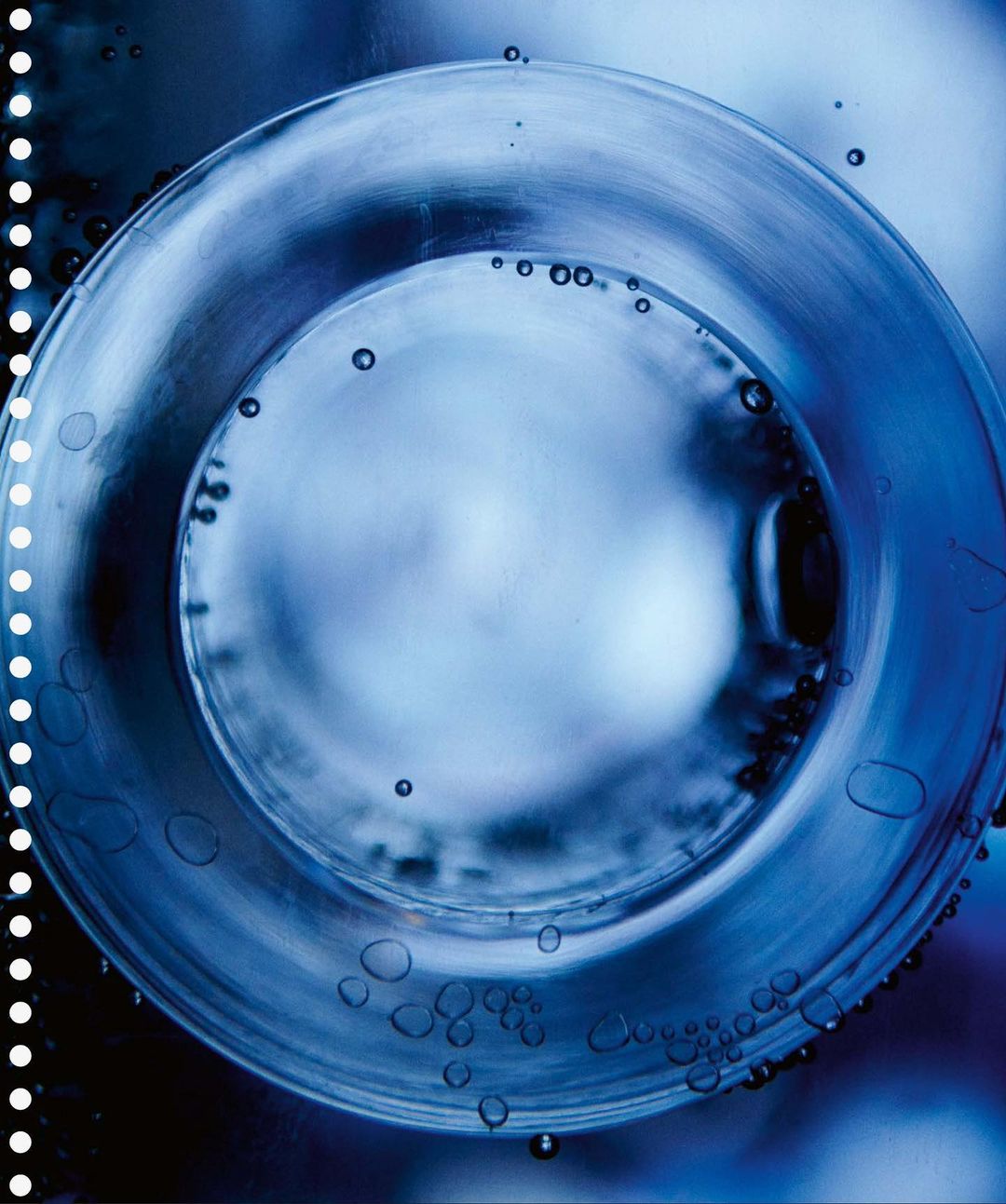 Close-up of a glass object underwater, surrounded by many small air bubbles, illuminated in blue tones, creating a sense of depth.
