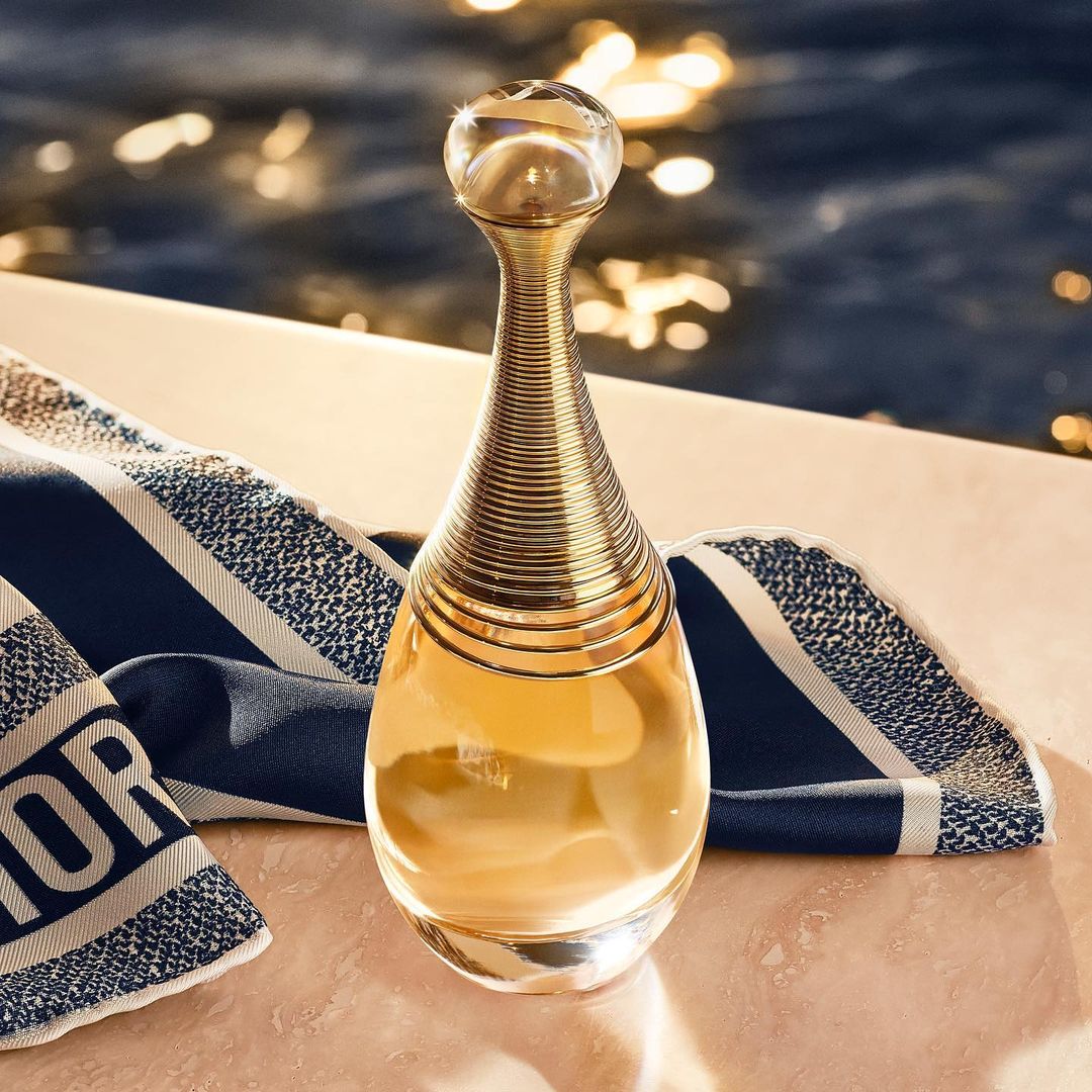 Perfume bottle of Dior's J'adore on a towel near a pool. Focus on the gold neck of the bottle, highlighting its elegance and design.
