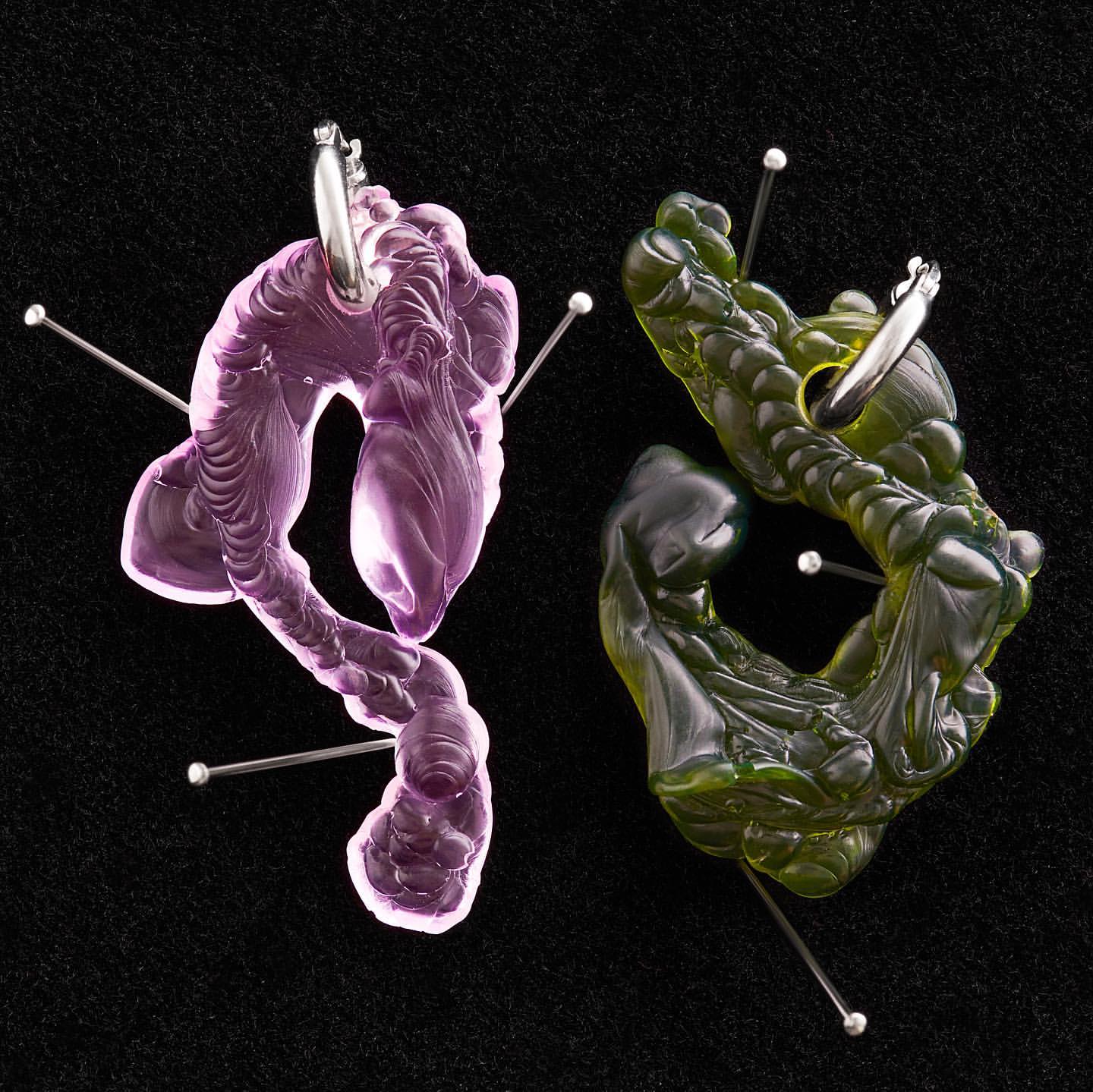 Abstract sculptures in pink and green with pins, displayed on a black surface, creating an artistic and textured visual composition.