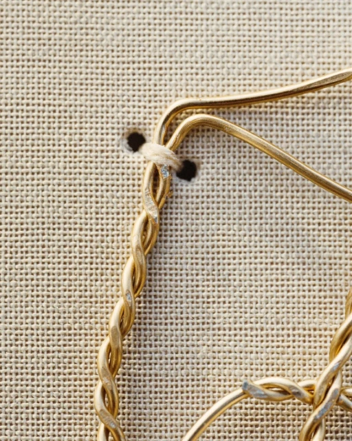 Close-up of a handmade gold wire art piece affixed to a beige fabric background featuring a twisted braid design.
