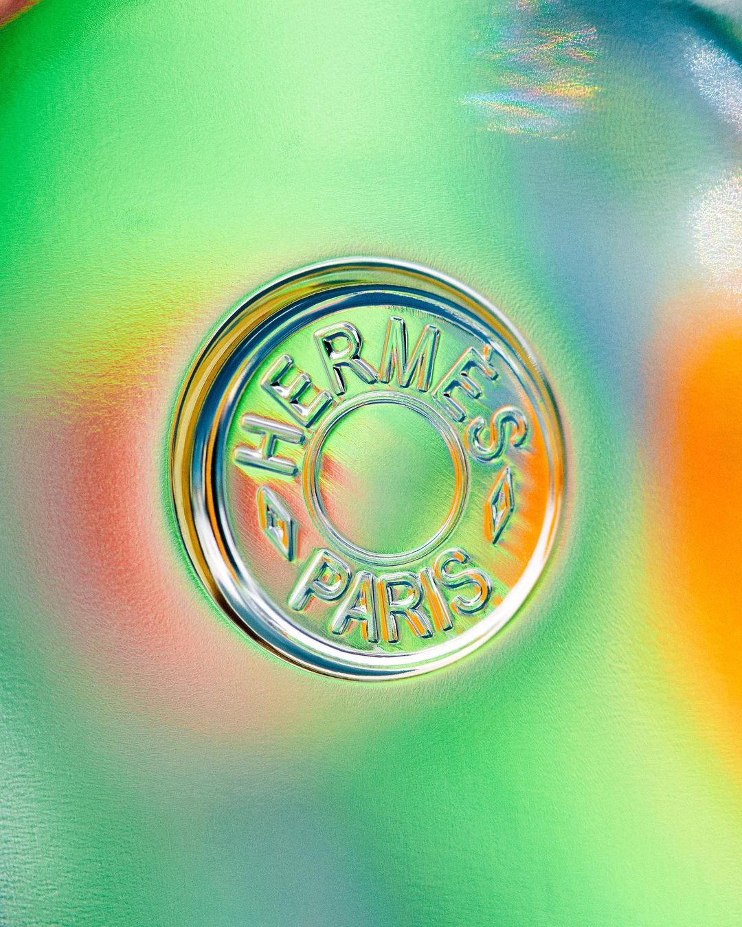 Close-up of an embossed Hermes Paris logo on a shiny surface with blended shades of orange, yellow, and green for luxury branding.
