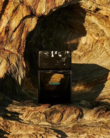 Dark rectangular perfume bottle with marbled white cap resting inside a hollow cavity of weathered wood.