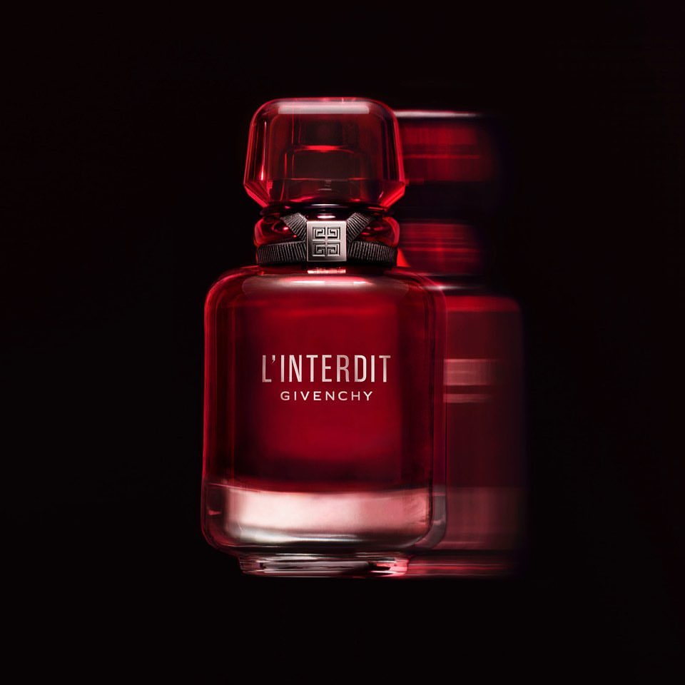 Close-up studio shot of a red glass Givenchy L'Interdit perfume bottle on a dark backdrop with a second bottle slightly blurred.