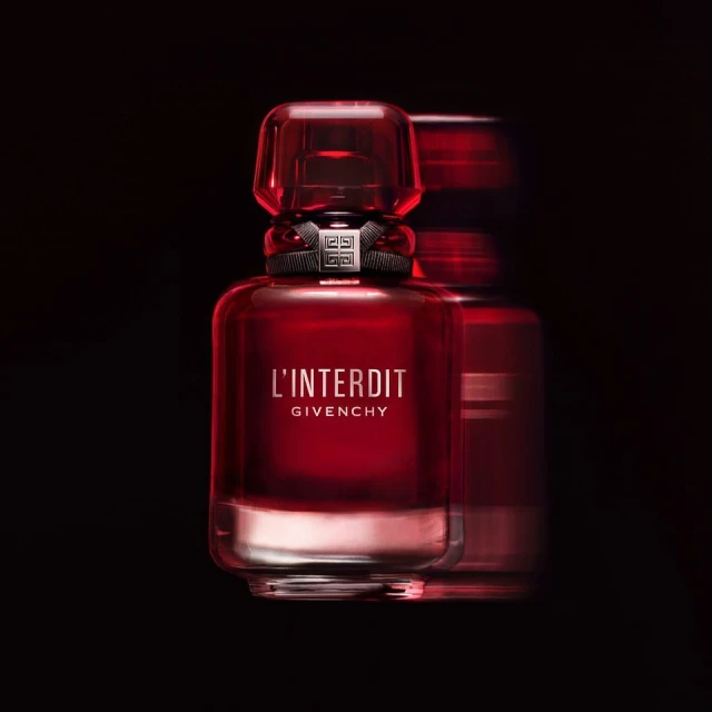 Close-up studio shot of a red glass Givenchy L'Interdit perfume bottle on a dark backdrop with a second bottle slightly blurred.