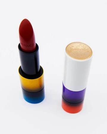 Hermes red lipstick with black and gold case open next to the white and purple lipstick case on a white background.