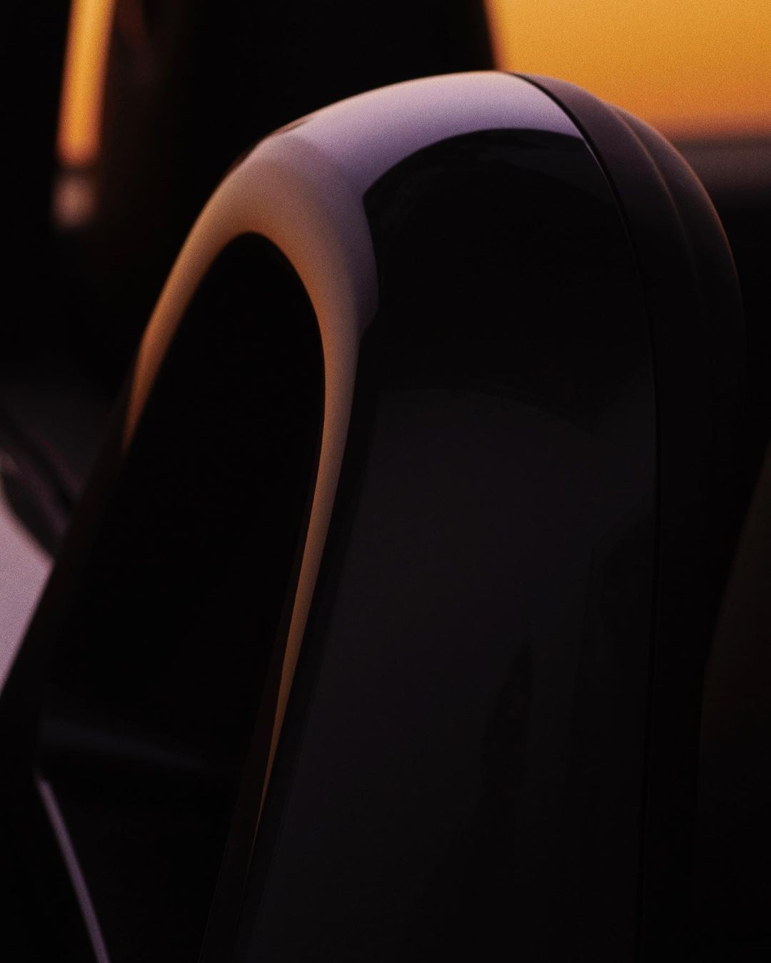 Close-up of a shiny, black automotive headrest in a car interior, catching light in a car interior with a sunset background.