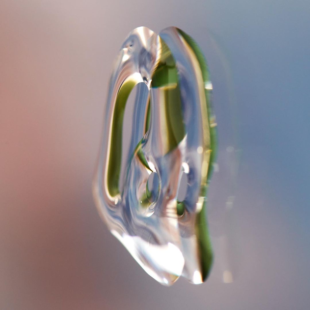 Abstract close-up of a clear, translucent object with green and blue reflections, set against a background gradient of peach and blue.